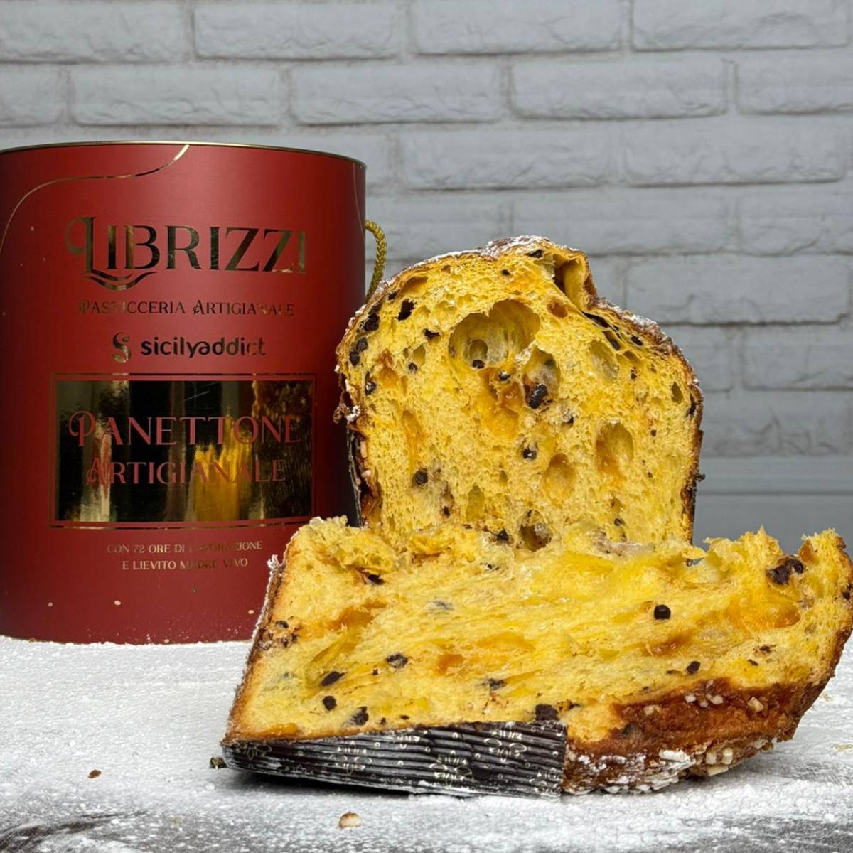 Panettone albicocca e cioccolato Librizzi Deluxe di SicilyAddict, tagliato con confezione davanti a una parete bianca